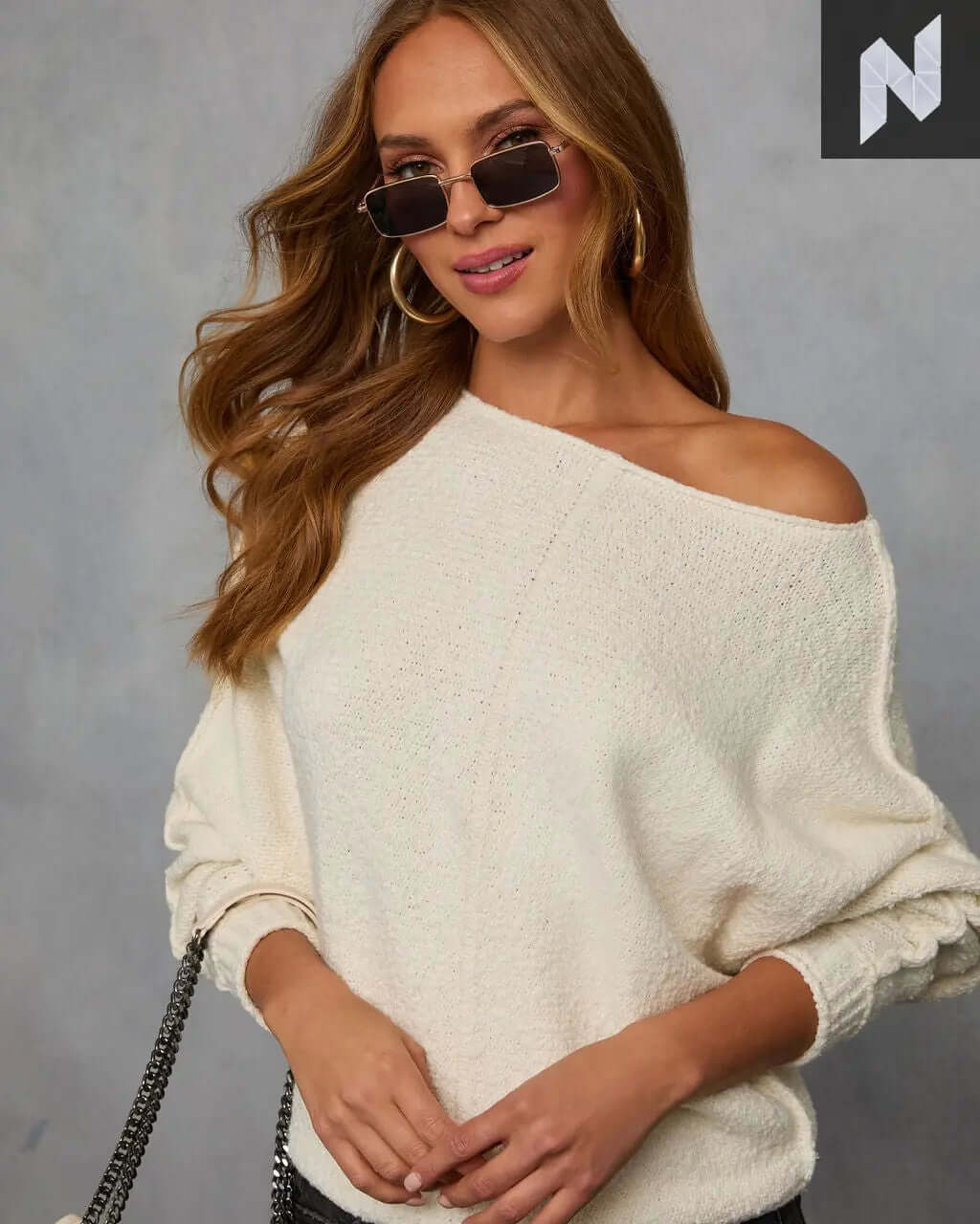 Woman wearing a cozy Avena Knit Sweater with off-shoulder design and stylish sunglasses, showcasing relaxed fashion.